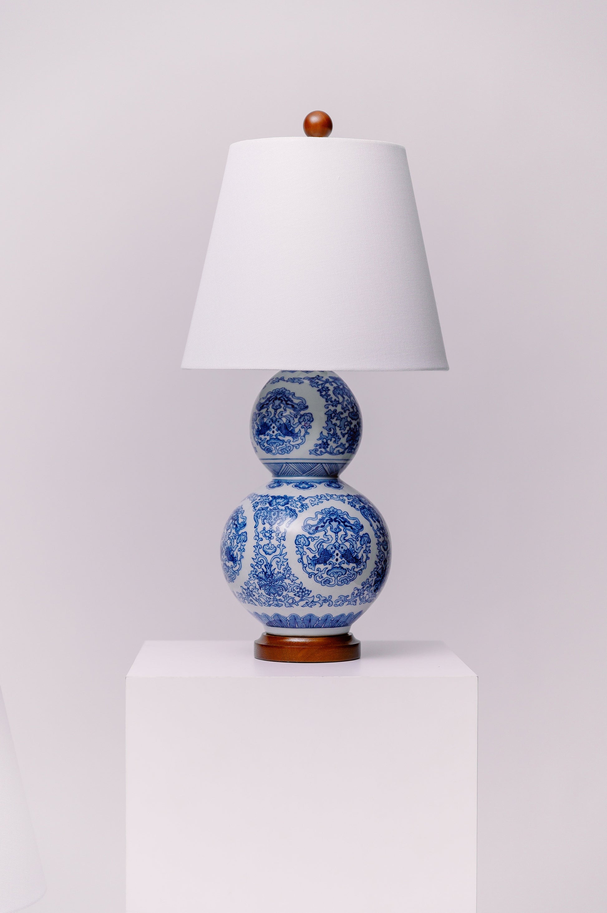 This pair of Ralph Lauren porcelain double gourd lamps features an intricate blue-and-white chinoiserie-inspired pattern on a classic silhouette. The bases are mounted on rich wood with brass-plated “Lauren” nameplates. Timeless in design and high in quality, these statement pieces add elegant symmetry to any traditional, coastal, or eclectic interior.  