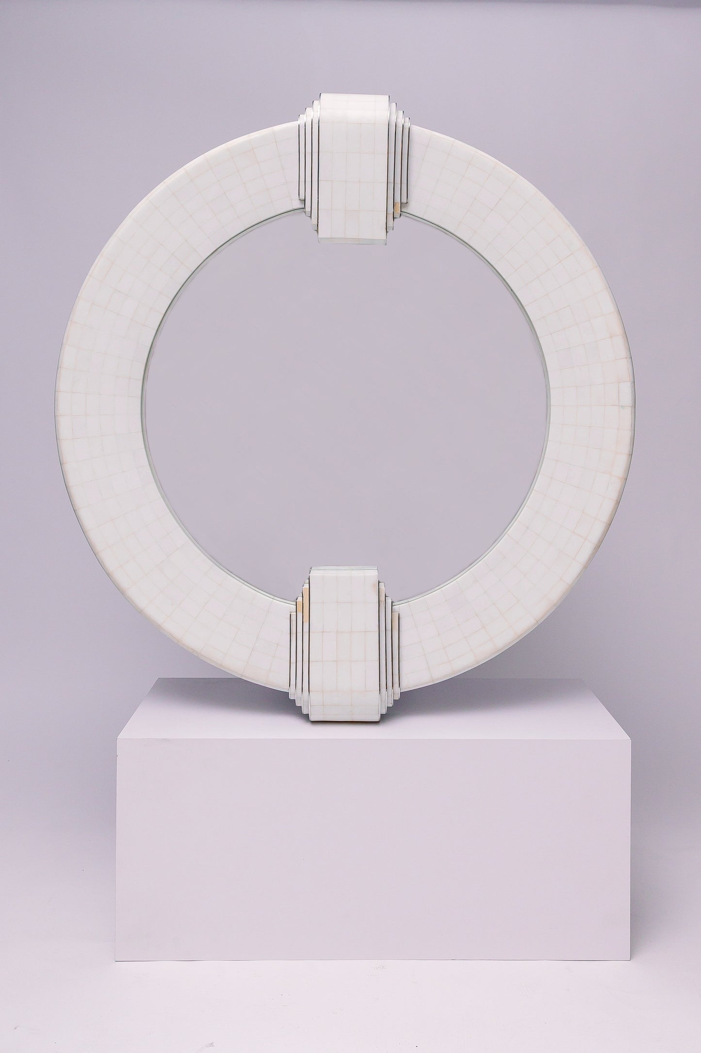 This mirror has a geometric, architectural feel with its bold circular frame, grid-like surface pattern, and stepped Art Deco–inspired detailing at the top and bottom. It feels both modern and timeless, almost like a sculptural piece.