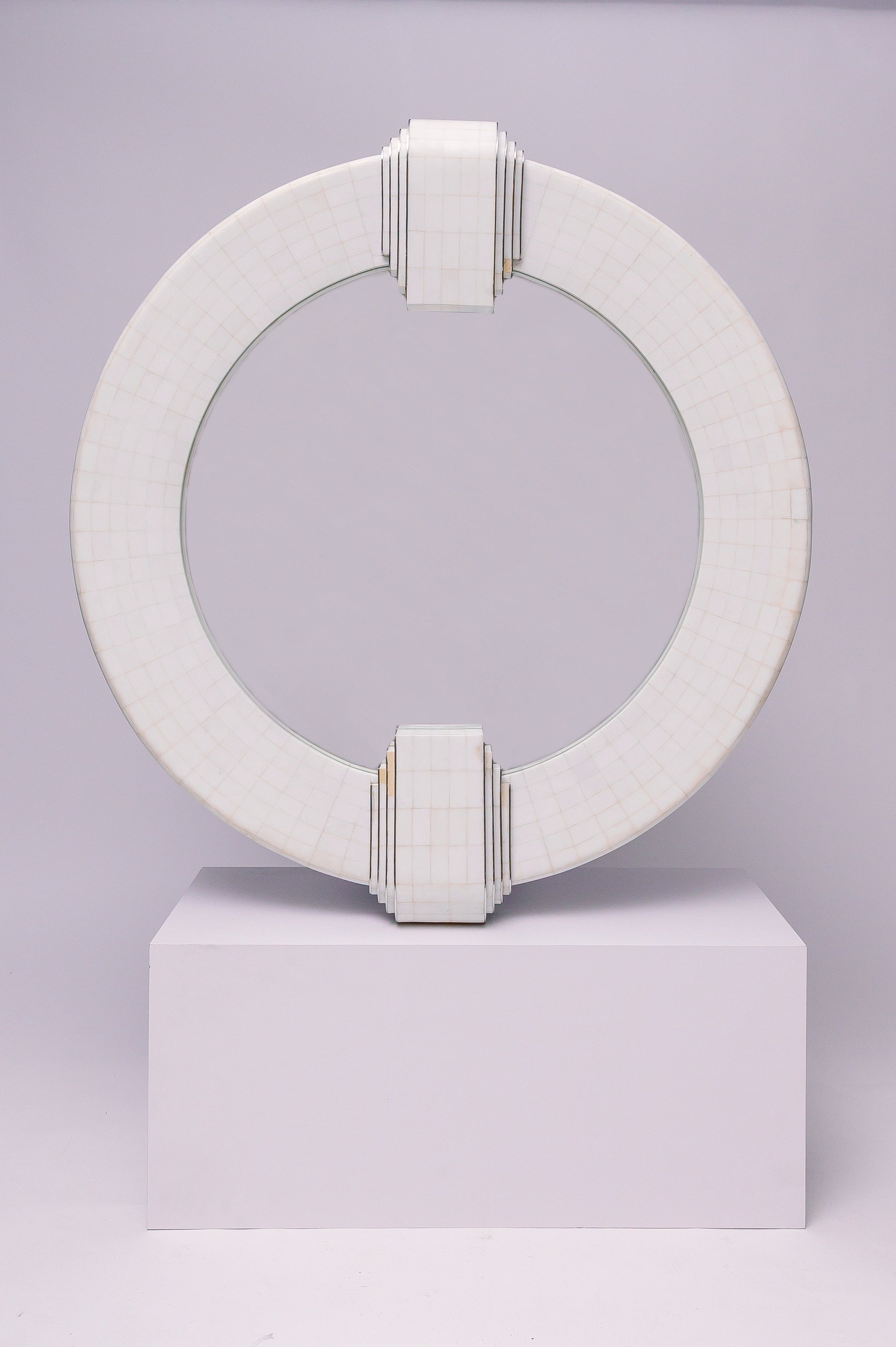This mirror has a geometric, architectural feel with its bold circular frame, grid-like surface pattern, and stepped Art Deco–inspired detailing at the top and bottom. It feels both modern and timeless, almost like a sculptural piece.