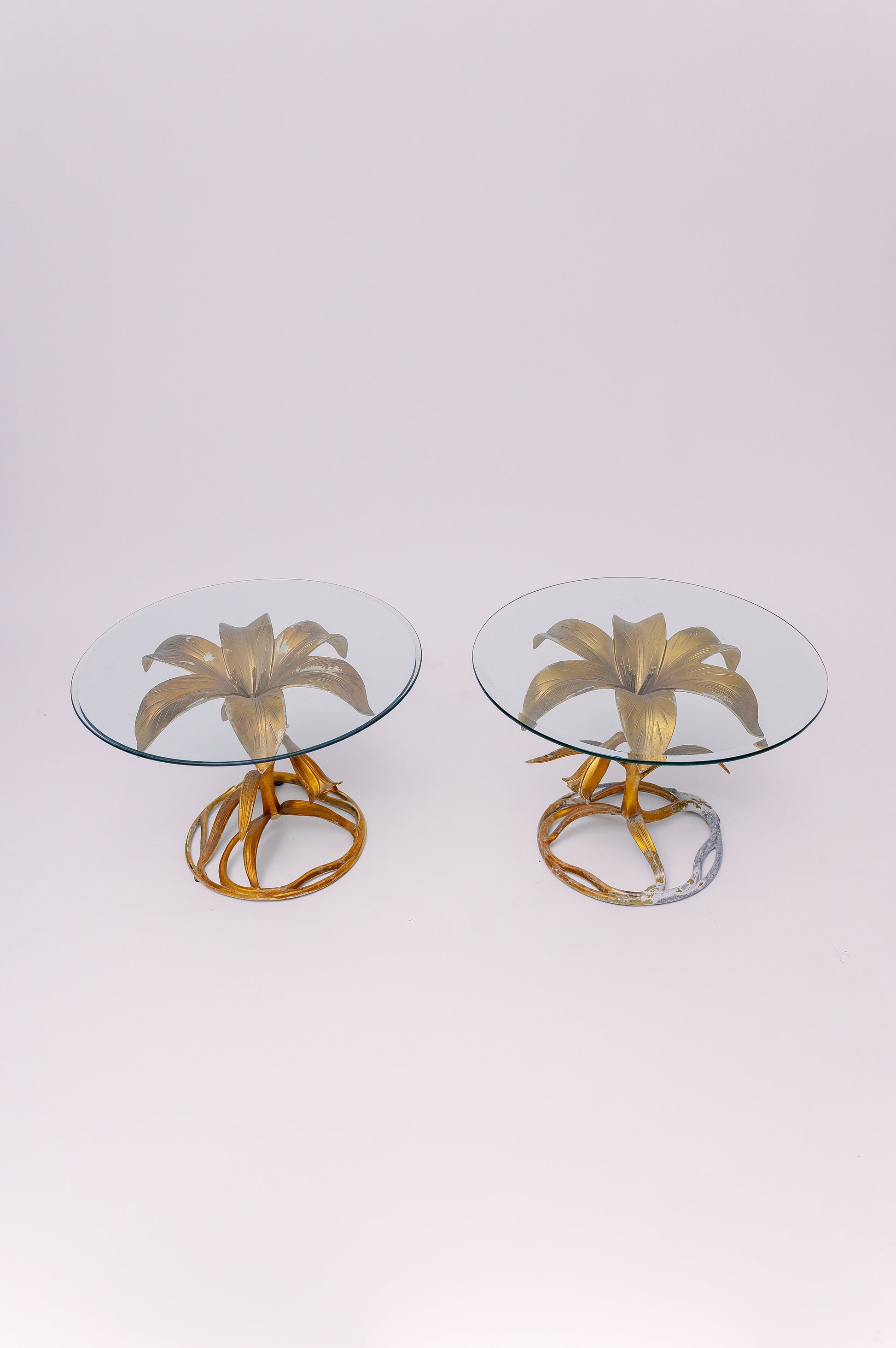 A pair of sculptural Mid-20th Century side tables by Arthur Court, featuring his iconic gilded lily motif in a radiant gold finish. The cast metal base blossoms upward into a bold floral form that supports a thick round glass top, adding organic elegance and Hollywood Regency charm to any space.