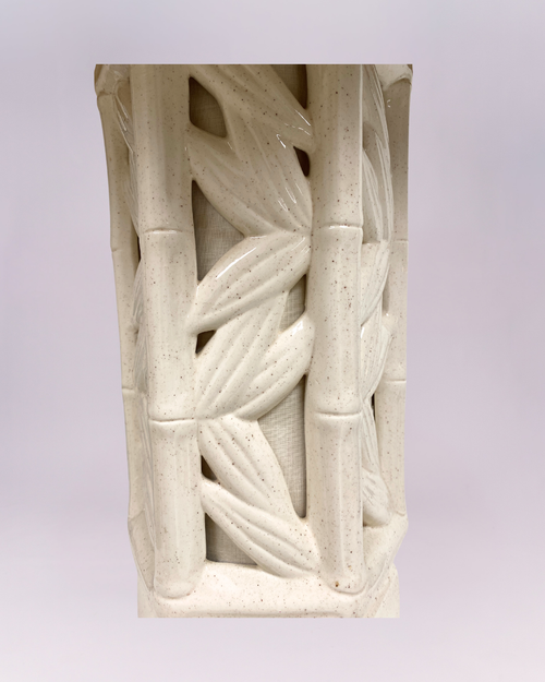 This is a statement table lamp featuring a cream-colored, octagonal ceramic or plaster base with a decorative openwork design that resembles woven bamboo or cane. It is topped with a large, pleated natural-tone fabric shade (like linen or raffia) that gives off a warm, diffused light.