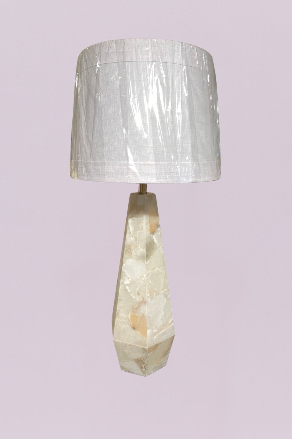 This sophisticated table lamp features a geometric, faceted base carved from natural quartz, showcasing a stunning array of organic veining in cream, white, and subtle earthy tones. The sharp, angular lines of the base provide a modern architectural feel, beautifully contrasted by the soft, clean silhouette of the white linen drum shade.