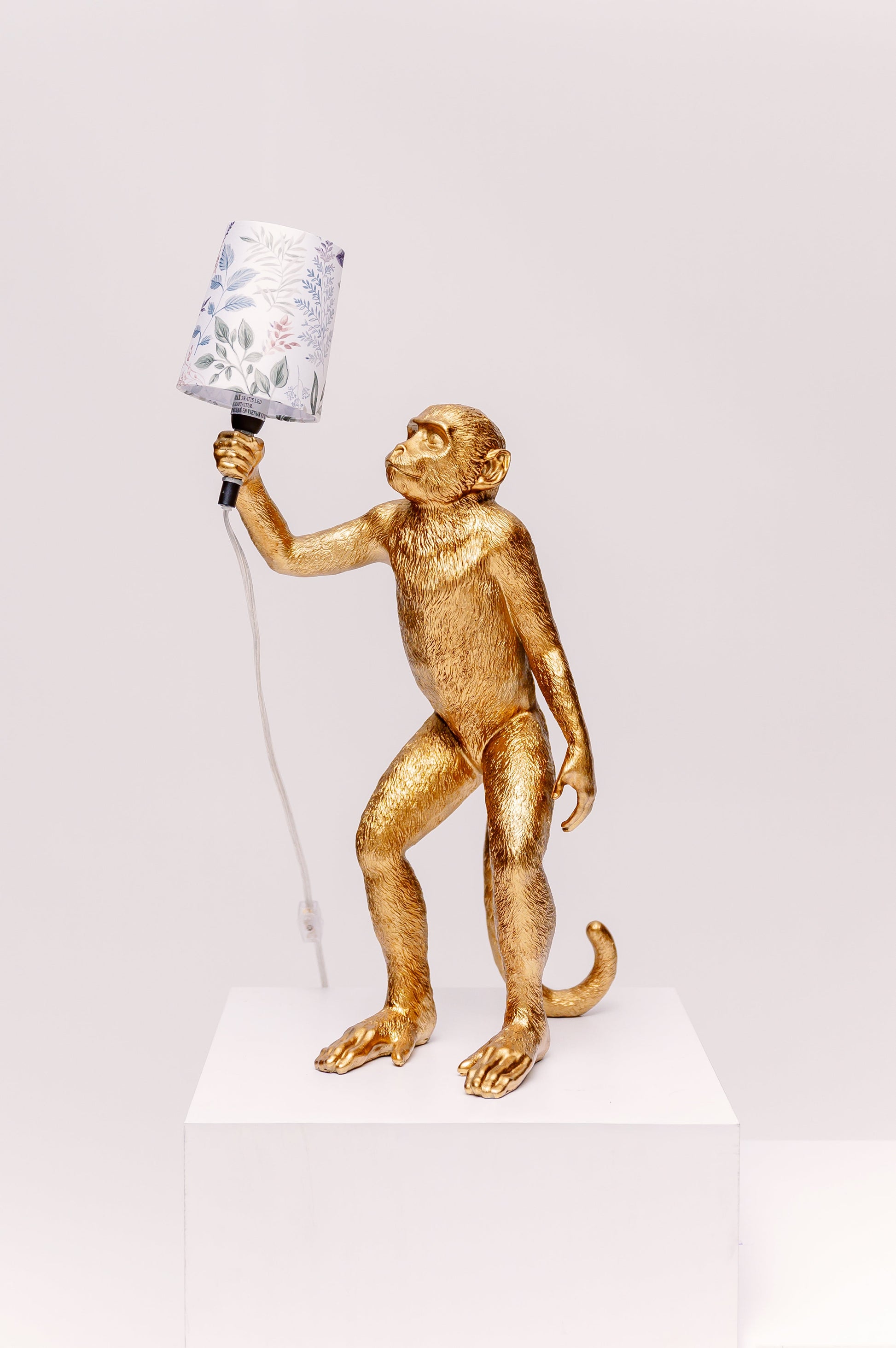Gold monkey lamp holding a lamp shade on a white background
