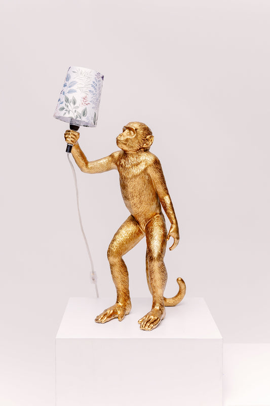 Gold monkey lamp holding a lamp shade on a white background