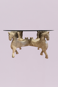 This striking statement piece features a meticulously detailed base composed of four hand-carved horses, creating a powerful and regal silhouette. The light, weathered finish highlights the intricate textural details of the carvings—from the flowing manes to the decorative saddles—giving the piece an antique, artisanal feel.