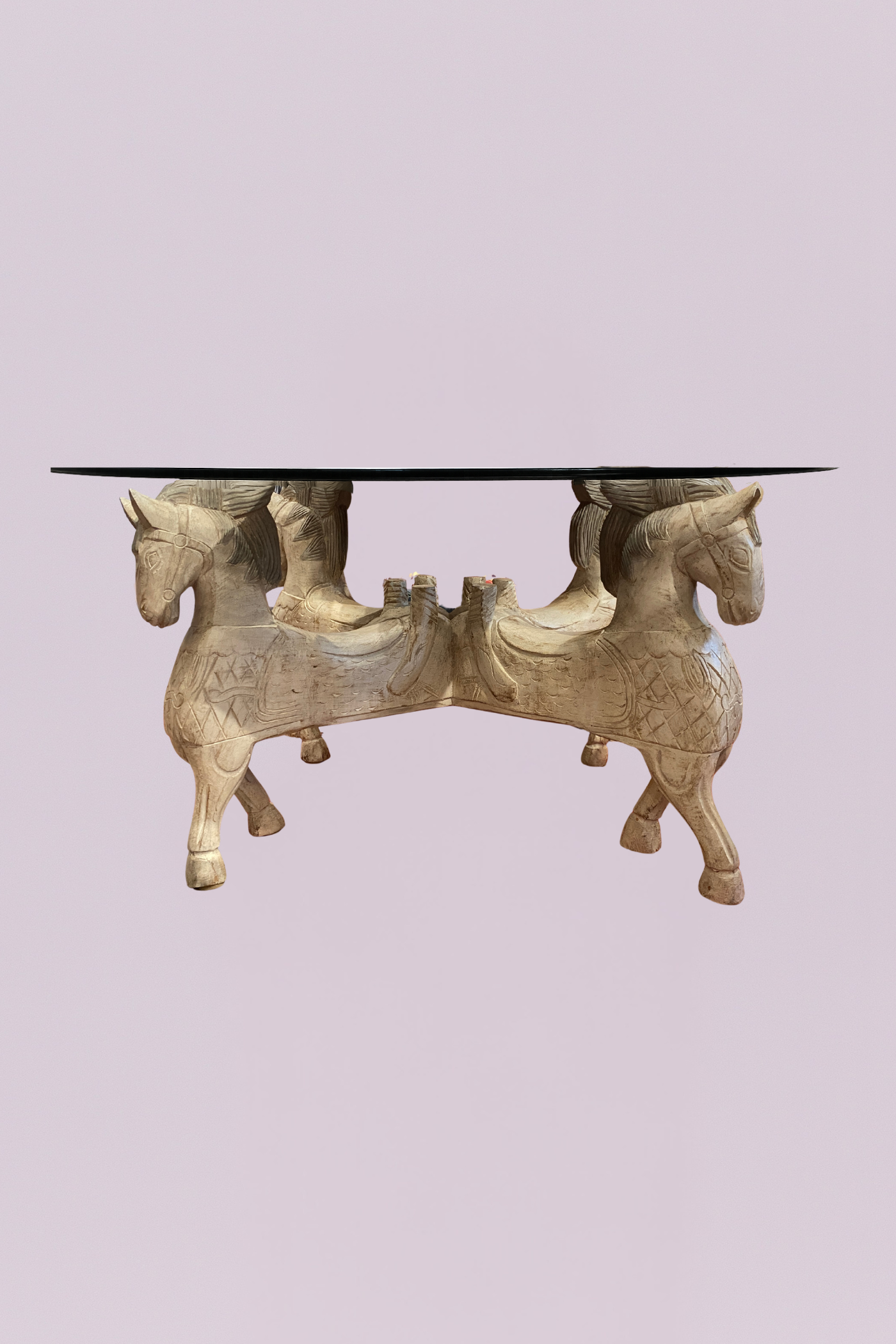 This striking statement piece features a meticulously detailed base composed of four hand-carved horses, creating a powerful and regal silhouette. The light, weathered finish highlights the intricate textural details of the carvings—from the flowing manes to the decorative saddles—giving the piece an antique, artisanal feel.
