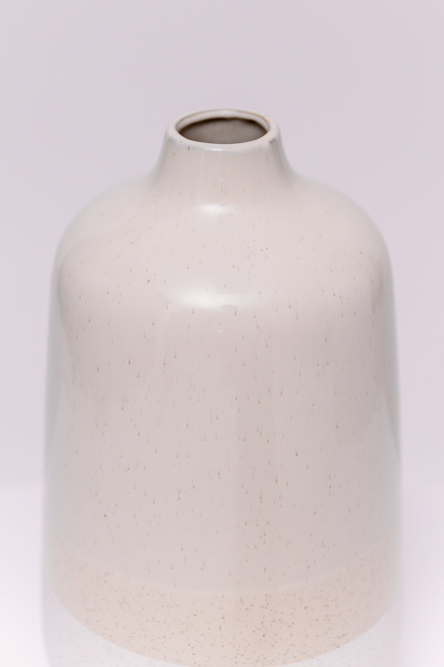 This minimalist stoneware vase features a clean cylindrical form with a soft taper at the neck. The body is finished in a natural two-tone glaze: a speckled white base, warm beige midsection, and soft taupe upper body, creating a subtle gradient effect. The matte texture and earthy palette lend a modern organic look, ideal for contemporary interiors.