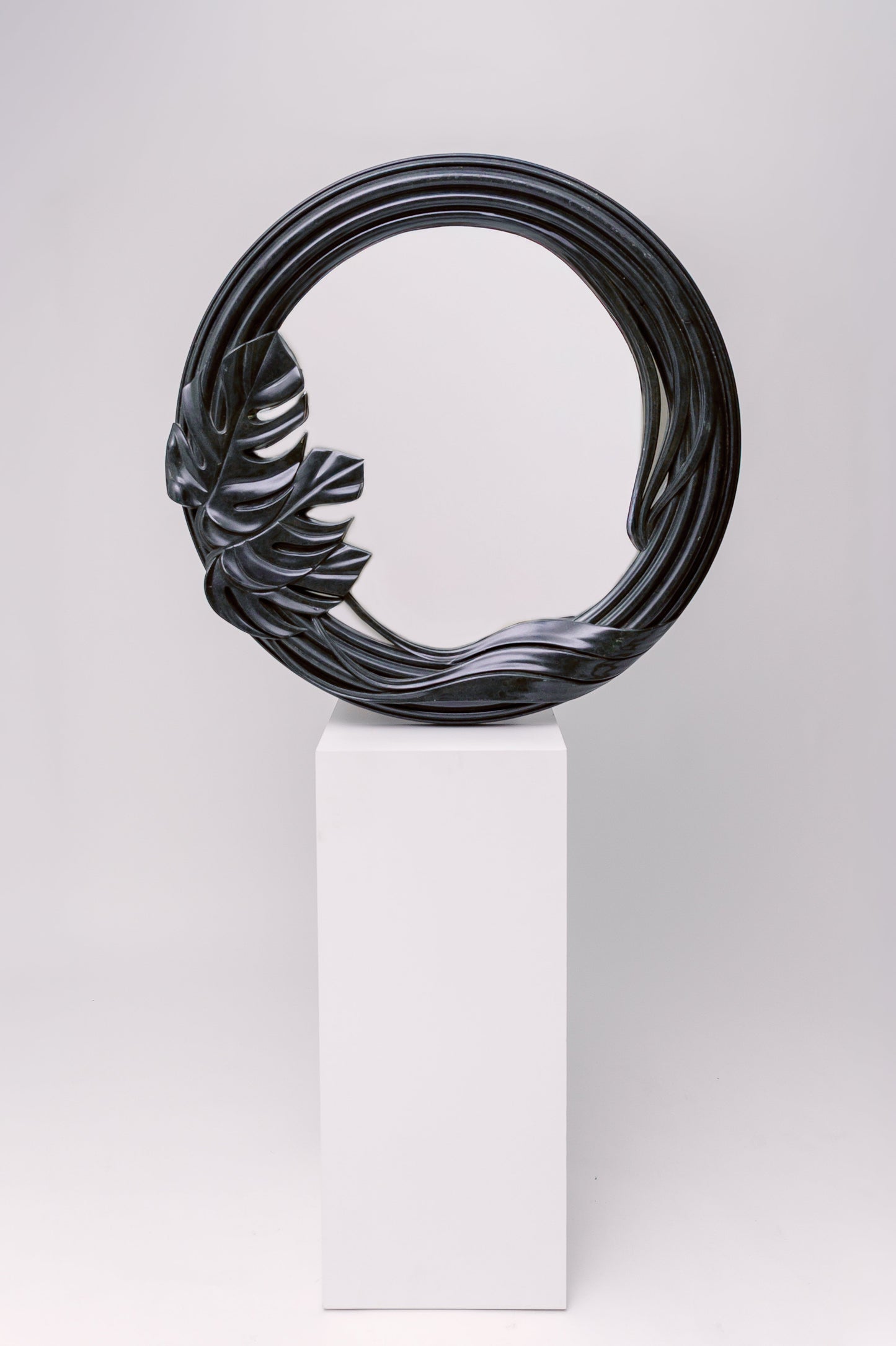 This mirror has a sculptural, organic frame with flowing curves and a carved tropical leaf detail, giving it a natural yet dramatic presence.