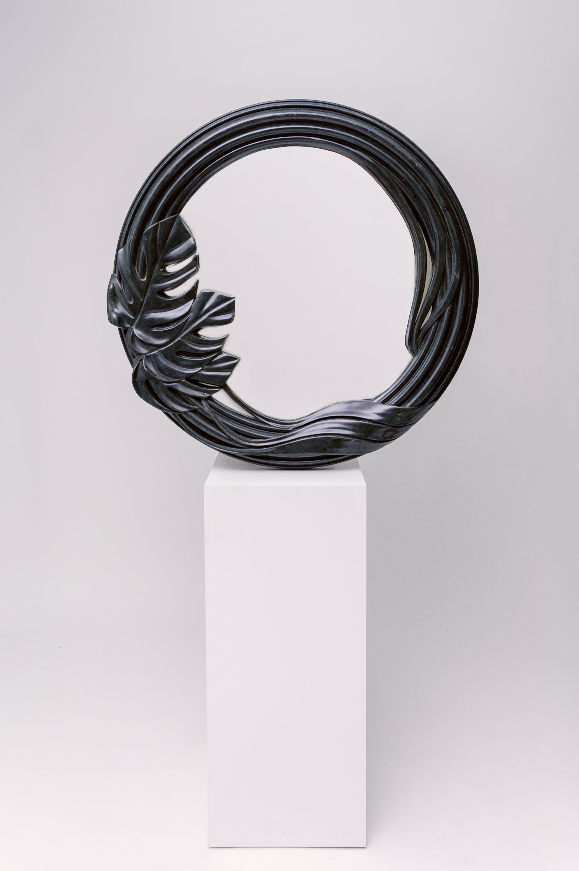 This mirror has a sculptural, organic frame with flowing curves and a carved tropical leaf detail, giving it a natural yet dramatic presence.