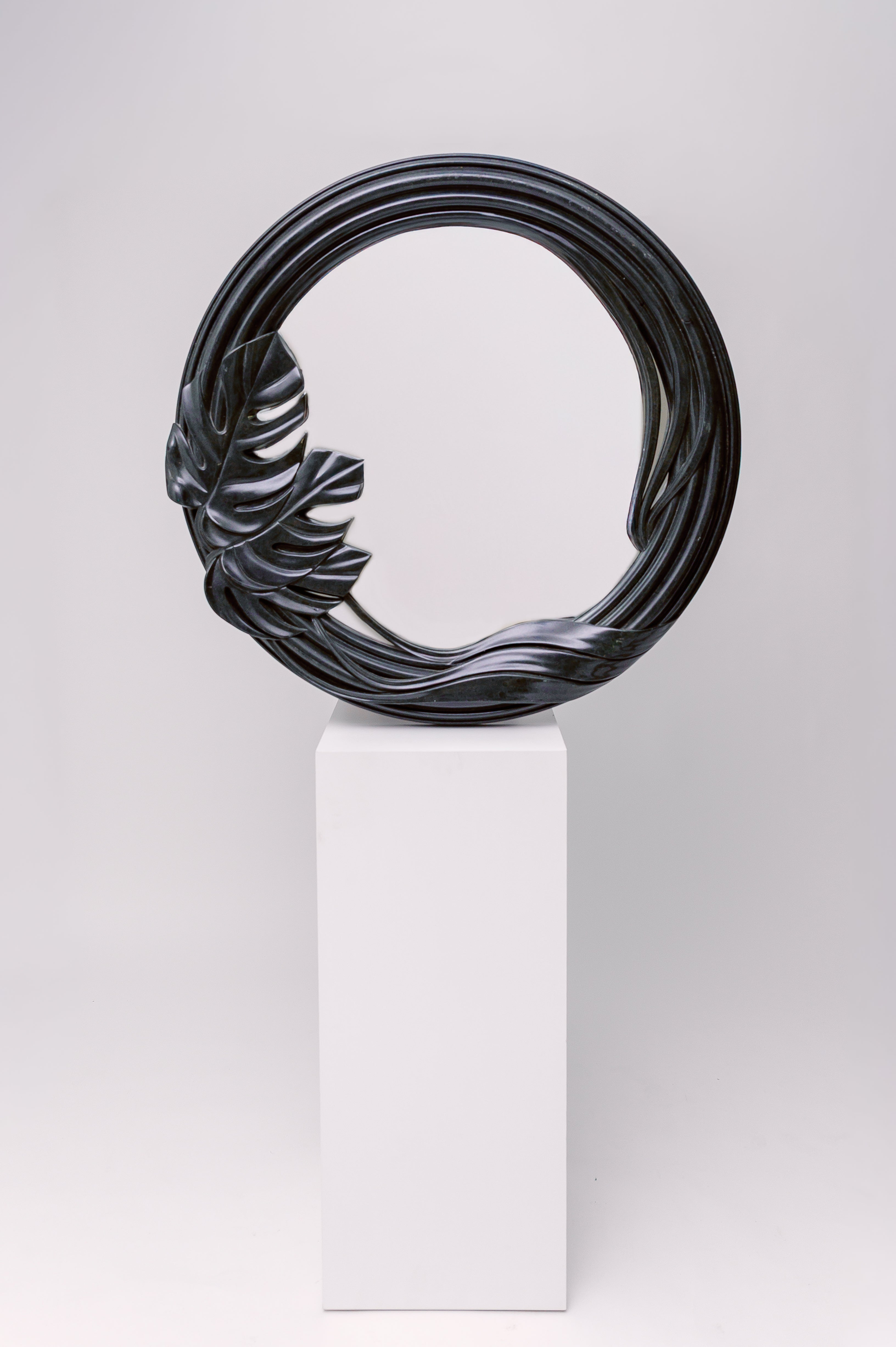 This mirror has a sculptural, organic frame with flowing curves and a carved tropical leaf detail, giving it a natural yet dramatic presence.