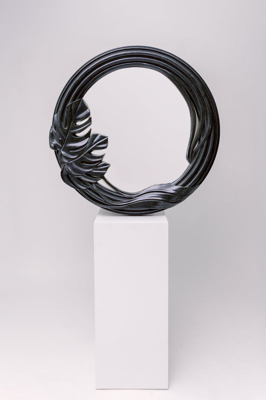 This mirror has a sculptural, organic frame with flowing curves and a carved tropical leaf detail, giving it a natural yet dramatic presence.