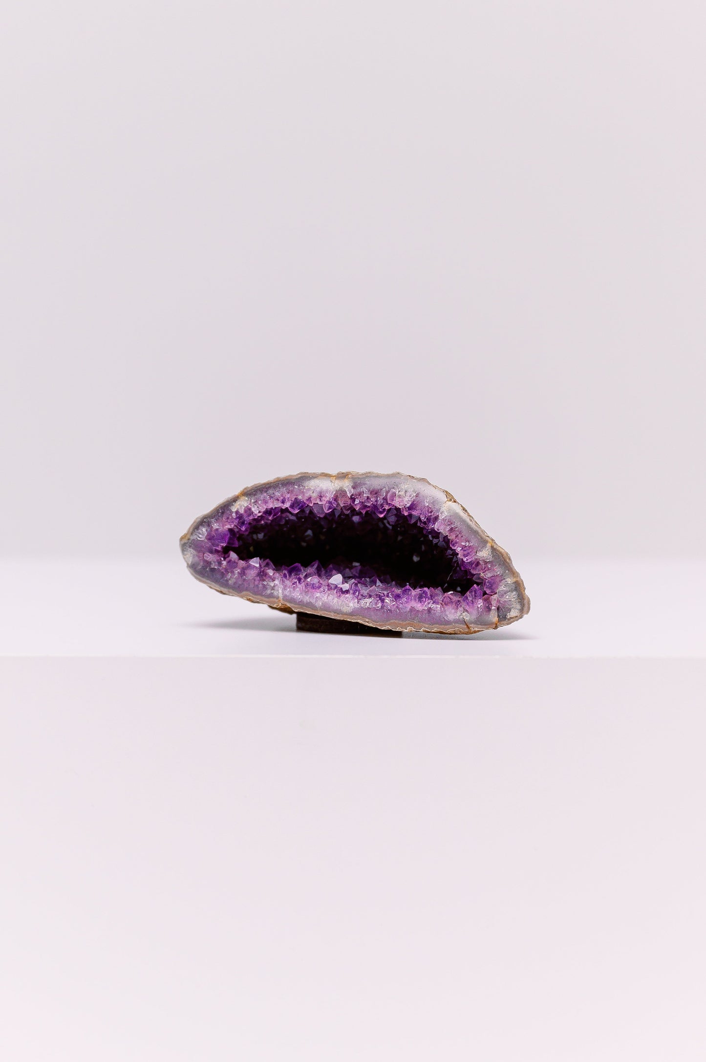 This is a stunning, natural amethyst geode that has been cut to reveal a cavity filled with sparkling, deep purple crystals. The outer layer of the geode is a rough, unpolished stone, which provides a striking contrast to the vibrant, polished crystals within. Sourced from regions known for high-quality amethyst, such as Uruguay or Brazil, this piece is a testament to the beauty of natural geological formations. Amethyst is a variety of quartz known for its calming energy, making this geode a perfect decora