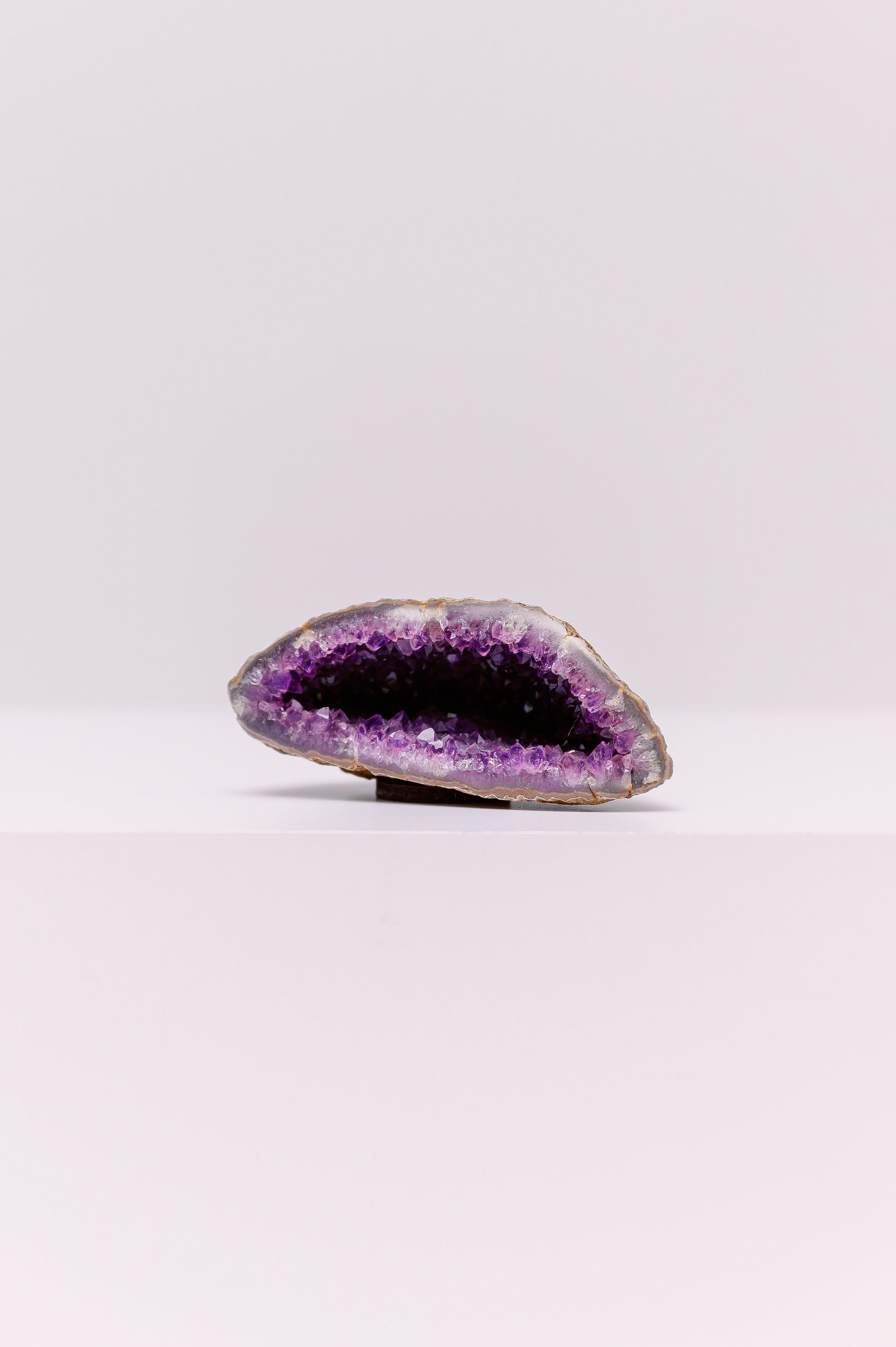 This is a stunning, natural amethyst geode that has been cut to reveal a cavity filled with sparkling, deep purple crystals. The outer layer of the geode is a rough, unpolished stone, which provides a striking contrast to the vibrant, polished crystals within. Sourced from regions known for high-quality amethyst, such as Uruguay or Brazil, this piece is a testament to the beauty of natural geological formations. Amethyst is a variety of quartz known for its calming energy, making this geode a perfect decora