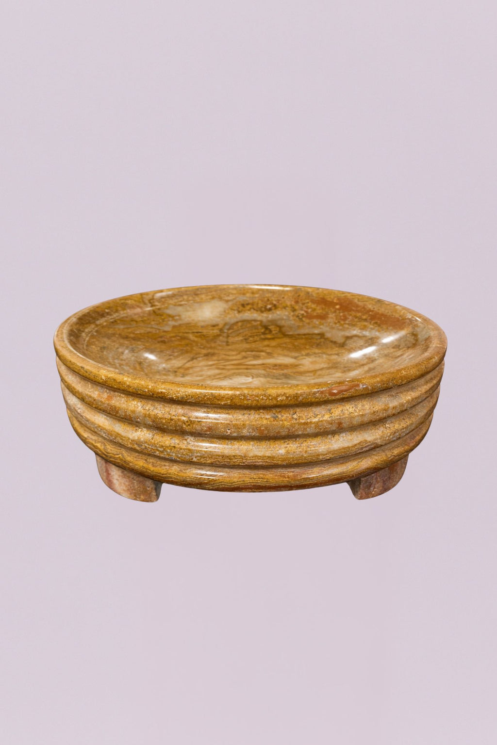 This elegant centerpiece bowl is carved from a single piece of natural stone, showcasing rich, swirling earth tones and a polished finish. The exterior features a distinctive triple-tiered ribbed design that adds a subtle architectural element to the piece, while the low, tripod-style feet provide a slight lift.