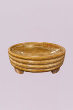 This elegant centerpiece bowl is carved from a single piece of natural stone, showcasing rich, swirling earth tones and a polished finish. The exterior features a distinctive triple-tiered ribbed design that adds a subtle architectural element to the piece, while the low, tripod-style feet provide a slight lift.