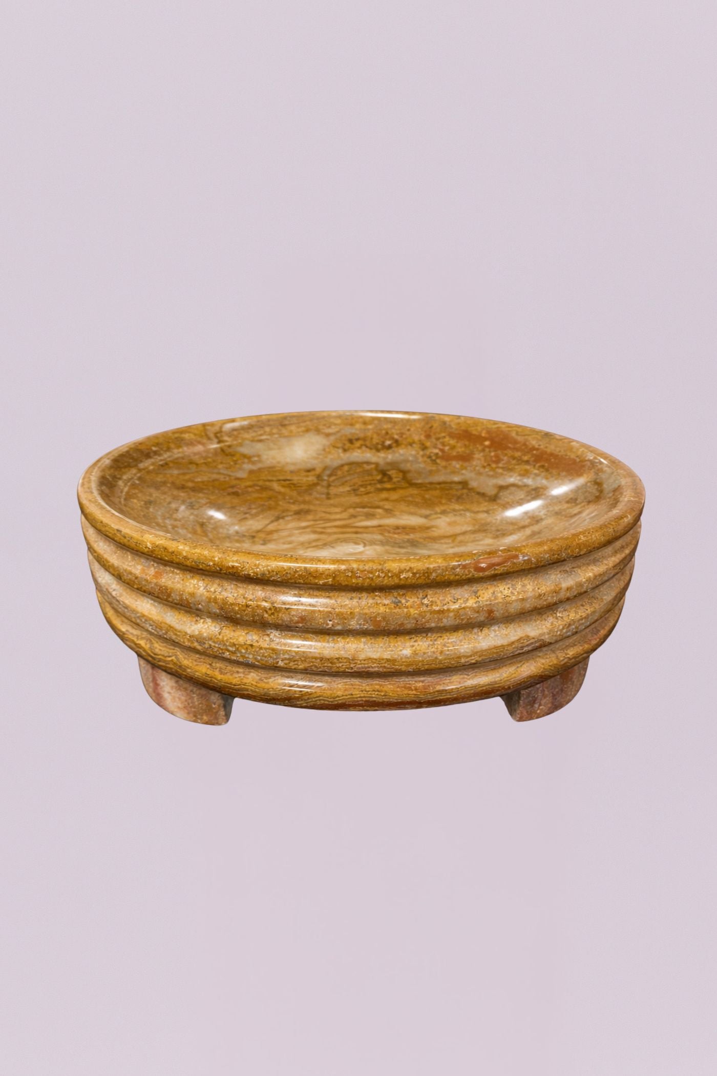 This elegant centerpiece bowl is carved from a single piece of natural stone, showcasing rich, swirling earth tones and a polished finish. The exterior features a distinctive triple-tiered ribbed design that adds a subtle architectural element to the piece, while the low, tripod-style feet provide a slight lift.
