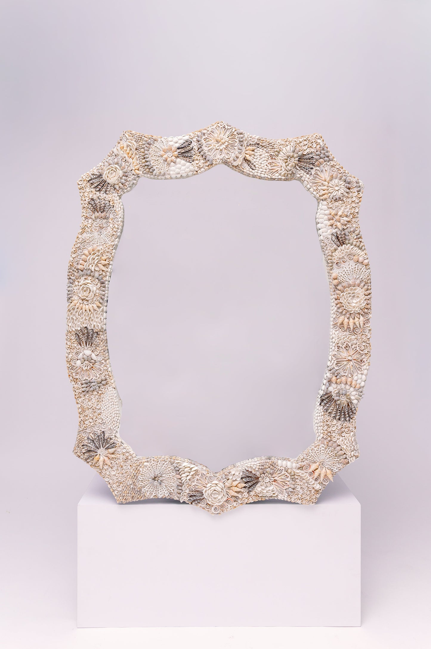 This  beautifully ornate mirror frame features intricate detailing made from seashells, arranged in floral and geometric patterns.