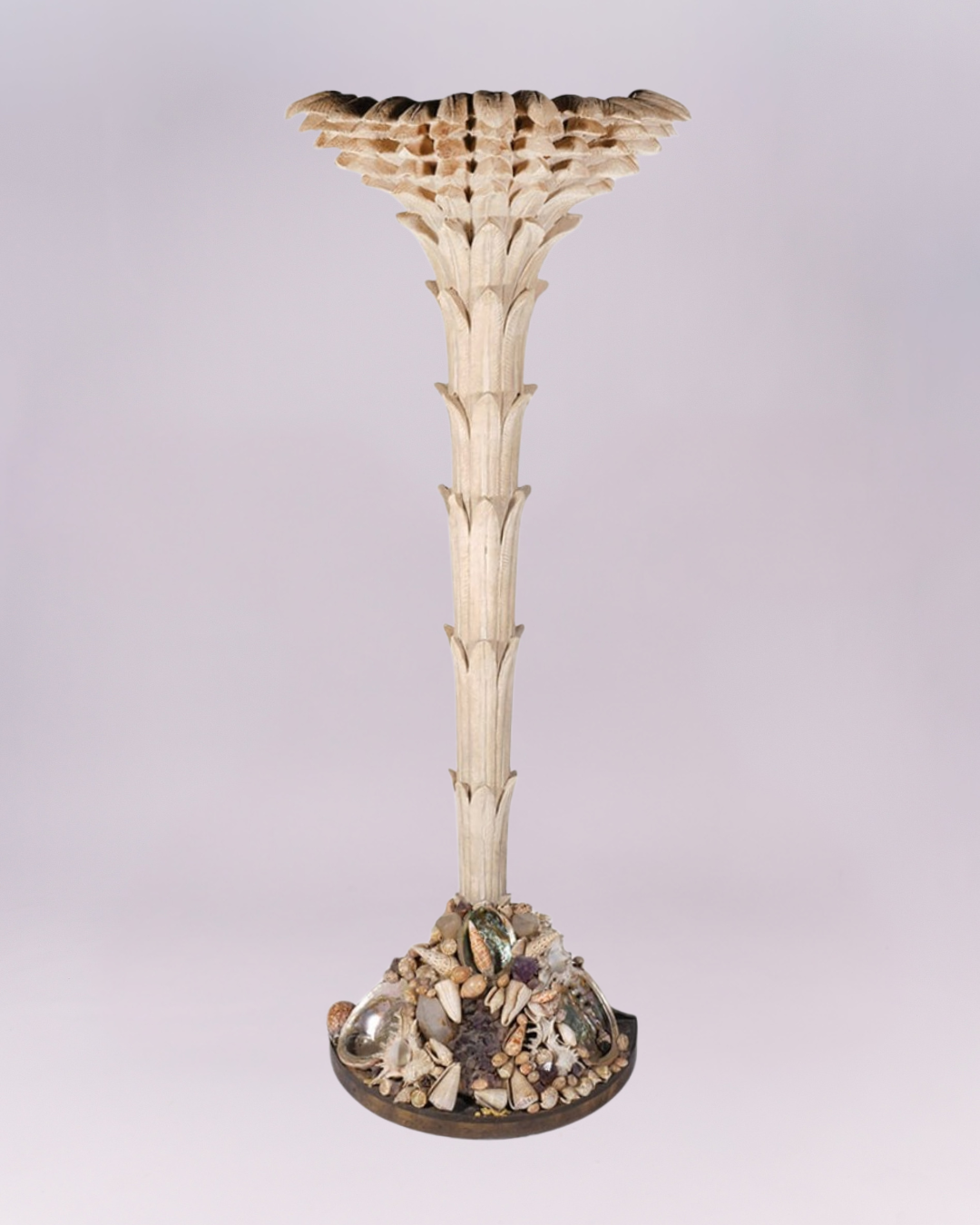 Carved wood palm tree Torchere attr. to Anthony Redmile has shell embelished base surmounted by carved wood form of a palm tree. Semi-circle metal base is covered with an assortment of sea shells in different shapes and sizes and measures 13"D x 22"W.  The tree form has wiring in the back and measures 74"H x 30"W top. 