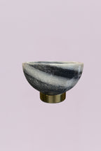 This elegant decorative bowl features a striking natural marble body with high-contrast grey and white veining. The organic, swirling patterns of the stone are beautifully offset by a clean, cylindrical base finished in a warm, brushed brass. Its compact scale makes it a sophisticated accent for smaller surfaces.