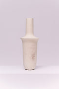 This striking vase features a tall, elongated silhouette with a cylindrical neck that flares into a broad collar before tapering to a rounded base. The matte off-white finish with subtle tonal variations gives it a raw, organic texture. Its sculptural form makes it a modern statement piece, ideal for display on its own or styled with tall branches or dried botanicals.