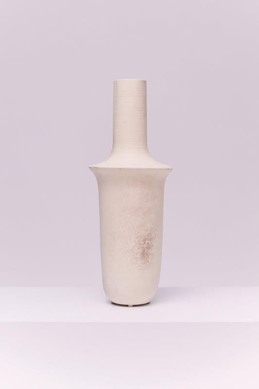 This striking vase features a tall, elongated silhouette with a cylindrical neck that flares into a broad collar before tapering to a rounded base. The matte off-white finish with subtle tonal variations gives it a raw, organic texture. Its sculptural form makes it a modern statement piece, ideal for display on its own or styled with tall branches or dried botanicals.
