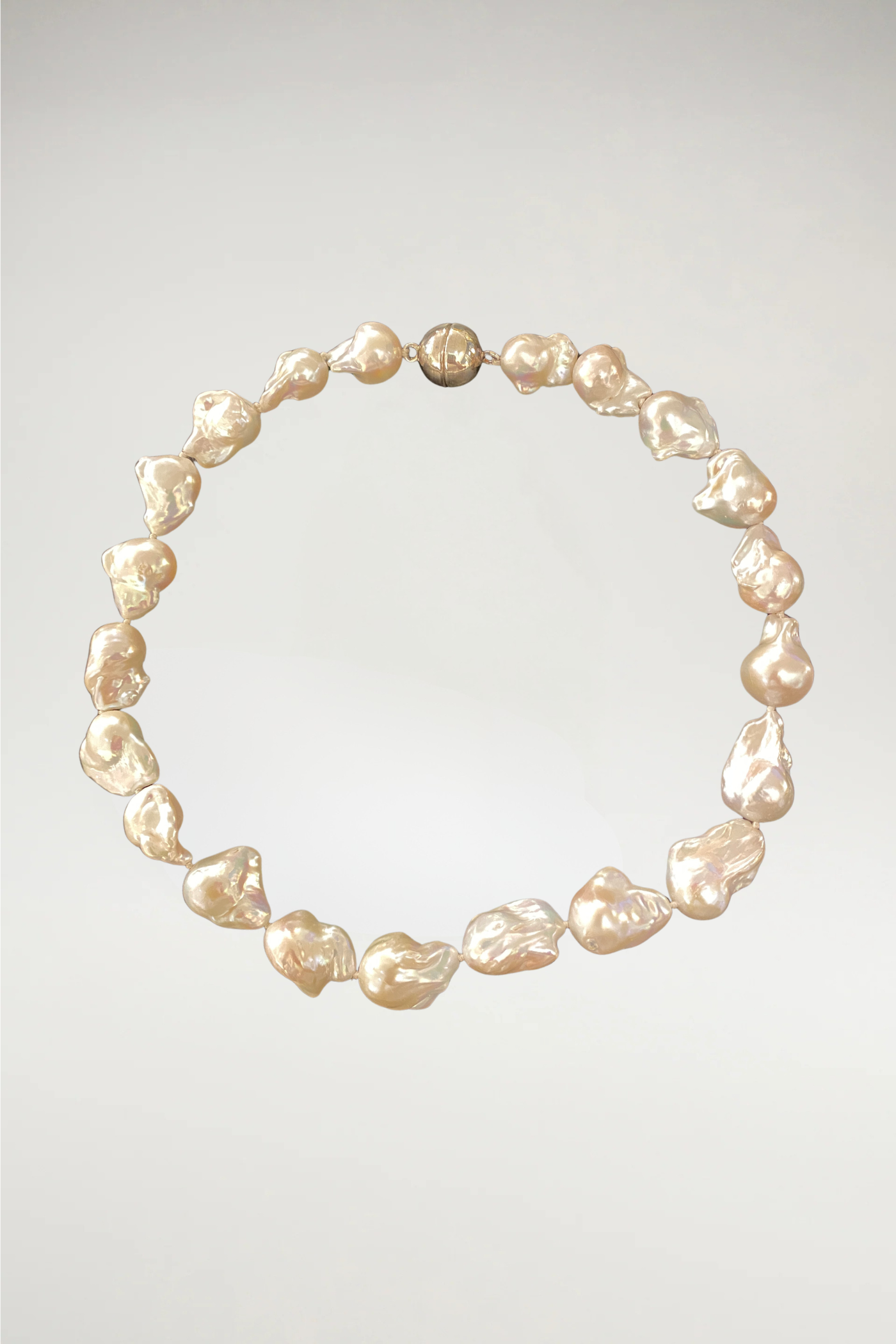 A majestic strand of oversized champagne baroque pearls. While The Eloise leans into cool, silvery-white tones, The Beatrice offers a warmer, more sun-kissed glow with deep honey and cream undertones. This piece is finished with a matching gold magnetic orb clasp to complement its rich, golden luster.