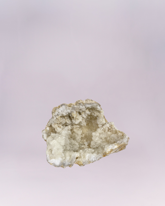 A mesmerizing natural wonder! This stunning geode fragment features a cave-like center lined with countless tiny, sparkling white and translucent quartz crystals, reminiscent of a frosty cavern. The rough, earthy stone shell provides a beautiful contrast to the bright, dazzling interior. Perfect for adding a touch of natural elegance and shimmer to any collection or display.