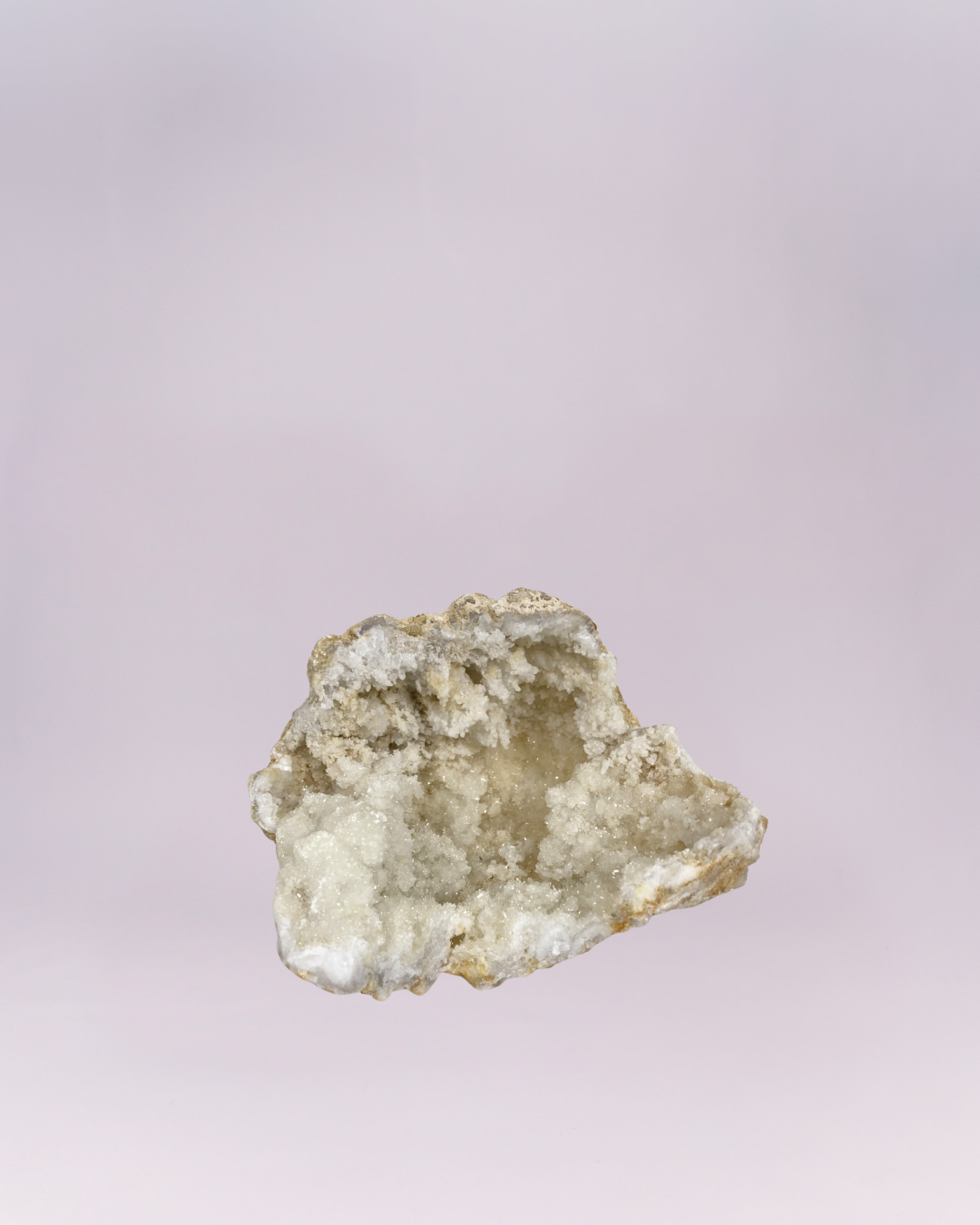 A mesmerizing natural wonder! This stunning geode fragment features a cave-like center lined with countless tiny, sparkling white and translucent quartz crystals, reminiscent of a frosty cavern. The rough, earthy stone shell provides a beautiful contrast to the bright, dazzling interior. Perfect for adding a touch of natural elegance and shimmer to any collection or display.
