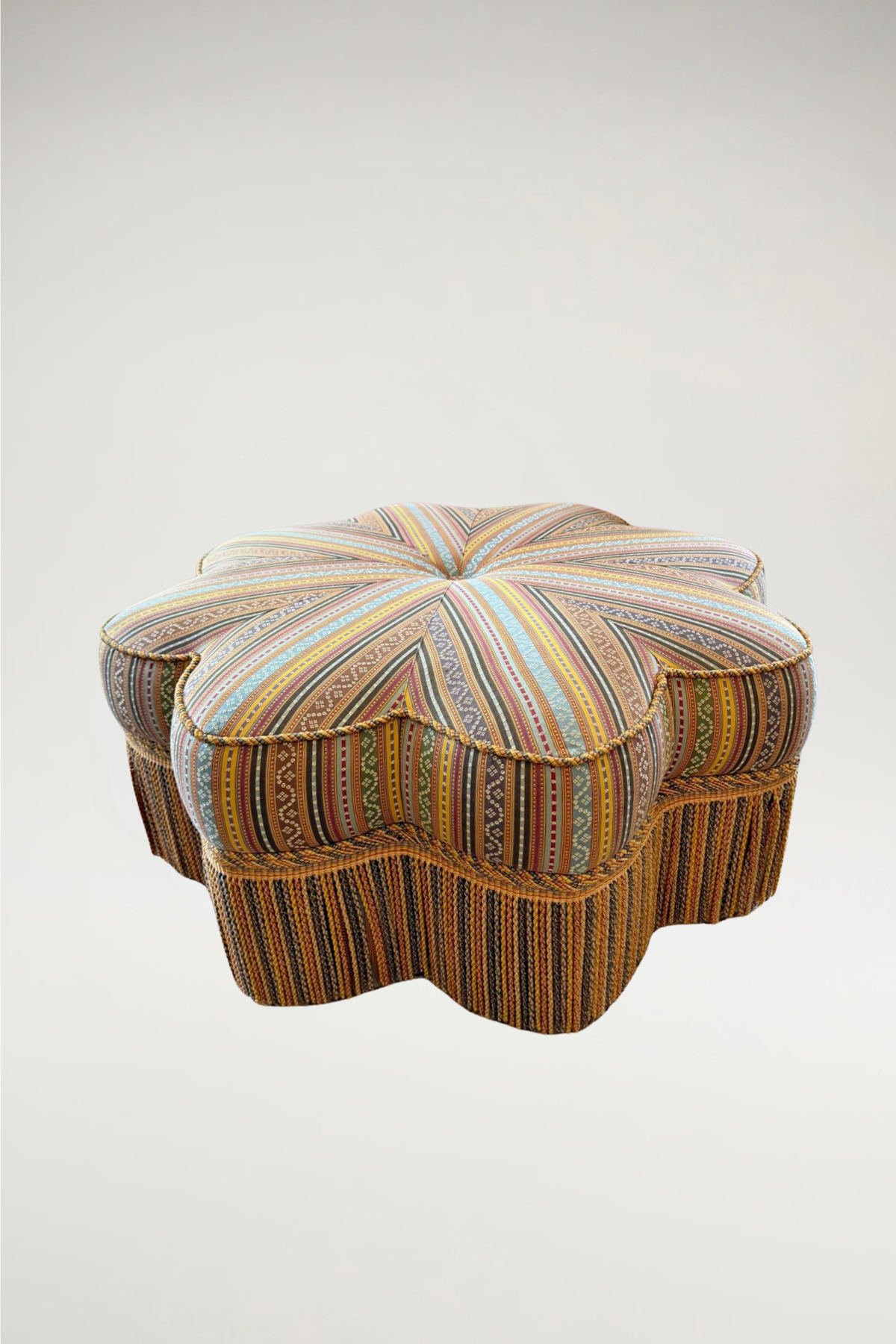 This piece is a masterful blend of whimsical geometry and traditional craftsmanship. Featuring a unique star-shaped silhouette, the ottoman is upholstered in a vibrant, multi-tonal striped textile that radiates from a central button tuft.