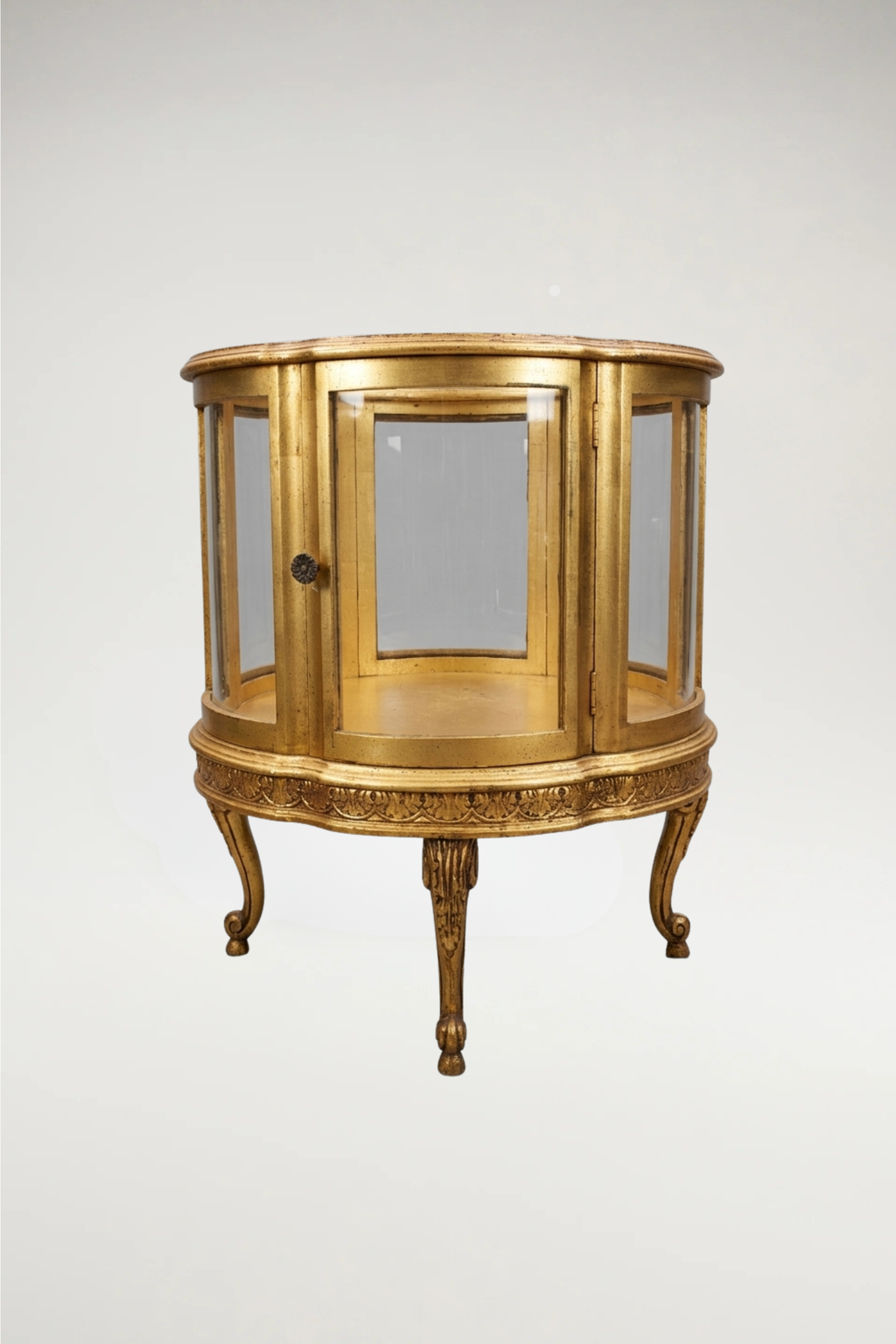 A sophisticated pair of  vintage circular display cabinets in the timeless Louis XVI style. Featuring a refined scalloped frame and a rich, aged-gilt finish, these vitrines offer an elegant, 360-degree view through seamless glass panels. Perfectly scaled for a moody, curated interior, they provide a regal stage for your most treasured collections