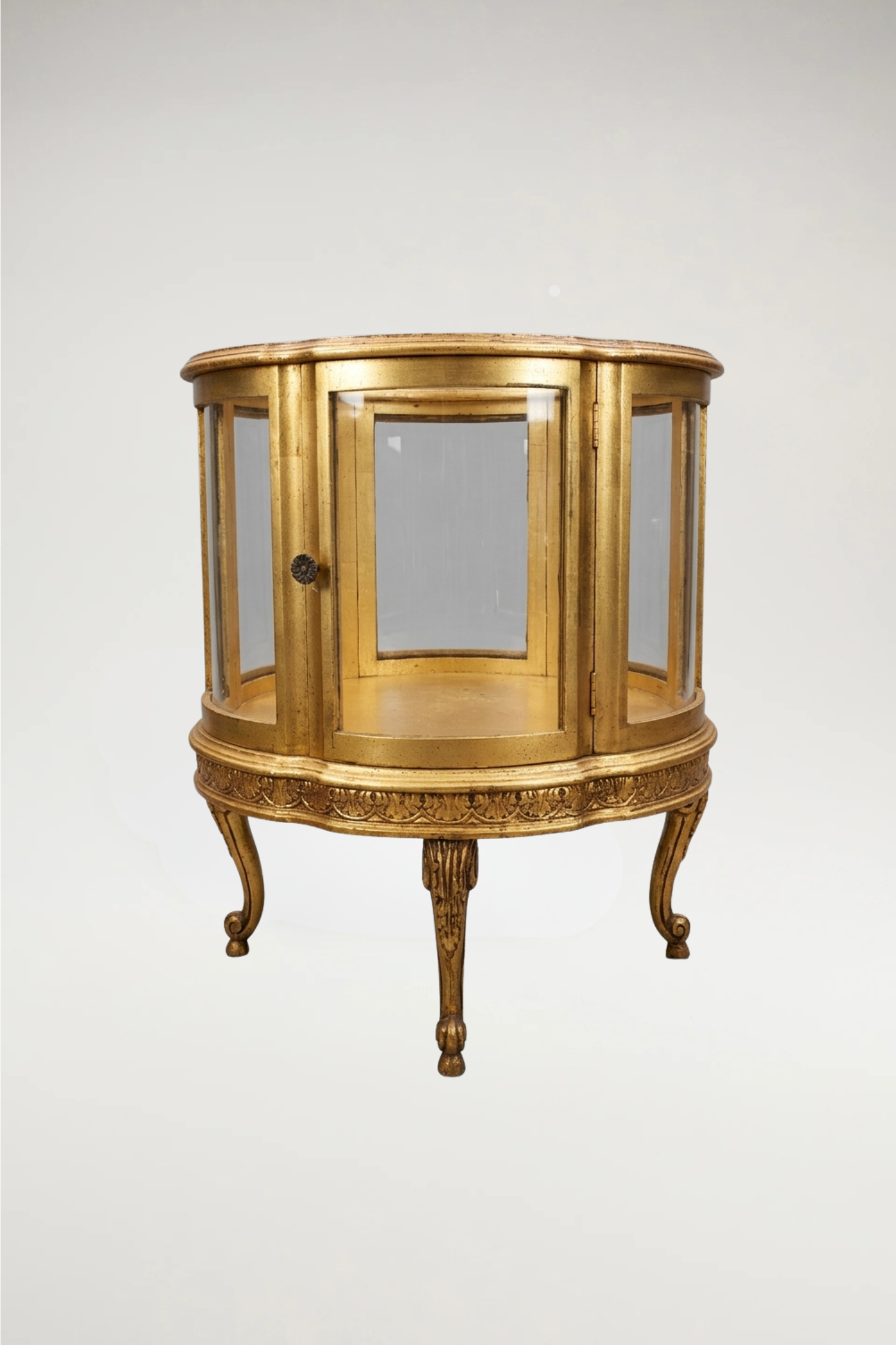 A sophisticated pair of  vintage circular display cabinets in the timeless Louis XVI style. Featuring a refined scalloped frame and a rich, aged-gilt finish, these vitrines offer an elegant, 360-degree view through seamless glass panels. Perfectly scaled for a moody, curated interior, they provide a regal stage for your most treasured collections
