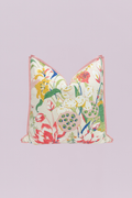 A vibrant botanical pillow featuring a waterlily and floral print in shades of red, yellow, green, and pink on a cream background, finished with a delicate pink piped edge.