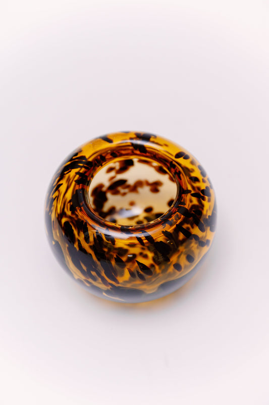 This sculptural art glass vase features a rounded bowl form with a striking tortoiseshell pattern in amber and deep brown. The swirling mottled effect creates rich depth and texture, while the smooth, high-gloss surface highlights the craftsmanship. Its wide opening and low, organic silhouette make it versatile for use as a vase, centerpiece, or decorative accent.