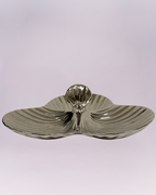 This is a highly reflective, three-section serving dish with a strikingly modern design. The piece features a triple-lobe, clover-like shape with a shallow central depression. The surface is heavily textured with a radial ripple or sunburst pattern, enhancing the metallic sheen of the material, which appears to be polished silver-toned metal or ceramic with a metallic glaze.