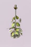 This charming vintage toleware table lamp features a delicate garden-inspired design, showcasing hand-painted white daisies and vibrant green foliage. The ivory-finished metal stem rises from a tiered circular base, with slender vines spiraling upward to support a cluster of botanical details.