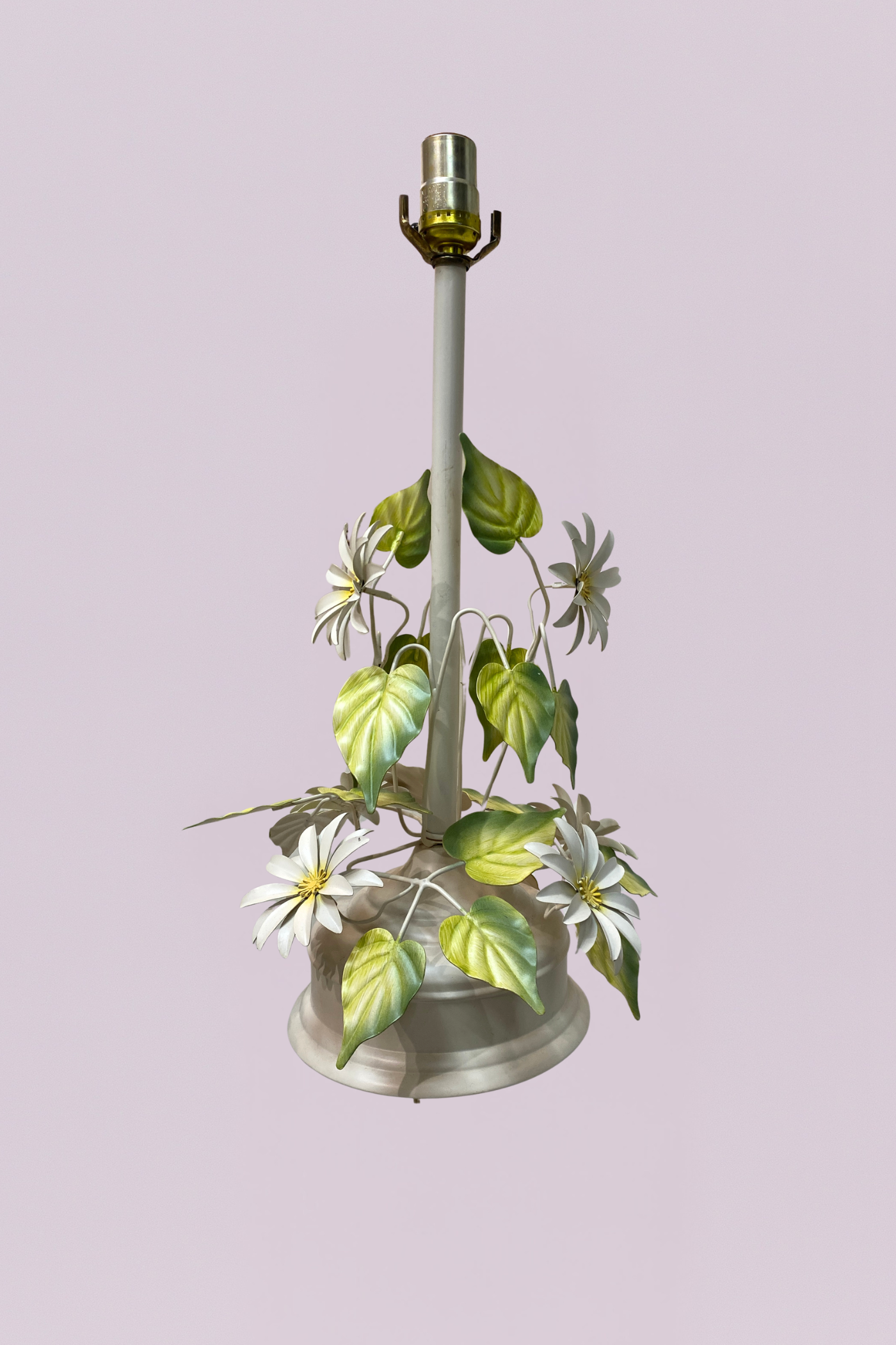 This charming vintage toleware table lamp features a delicate garden-inspired design, showcasing hand-painted white daisies and vibrant green foliage. The ivory-finished metal stem rises from a tiered circular base, with slender vines spiraling upward to support a cluster of botanical details.