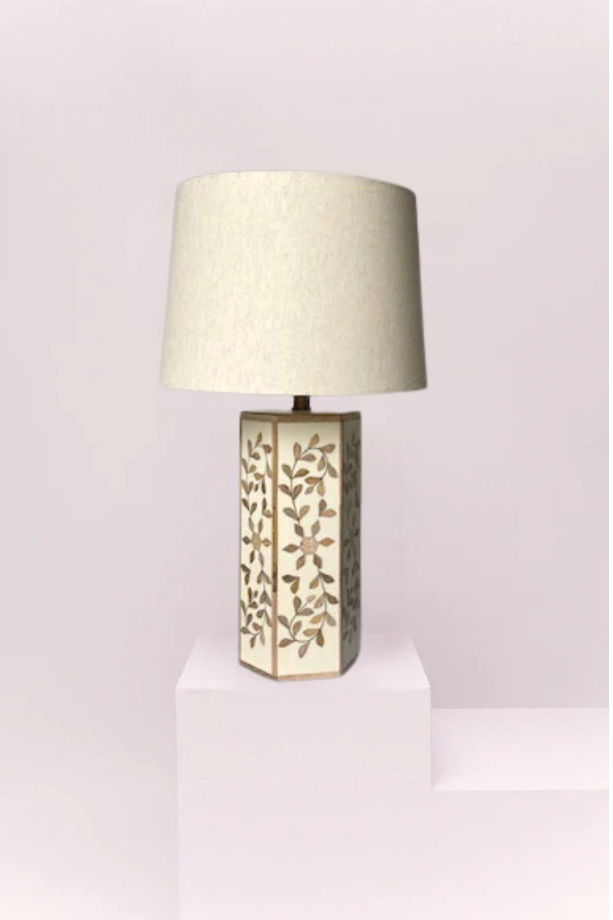 Table lamp with decorative base on a white pedestal against a gray wall